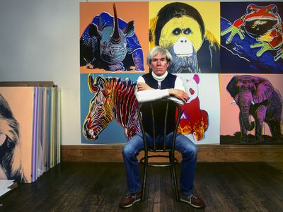 Pop artist Andy Warhol sits in front of artworks at his studio, the Factory, in New York City in 1983.