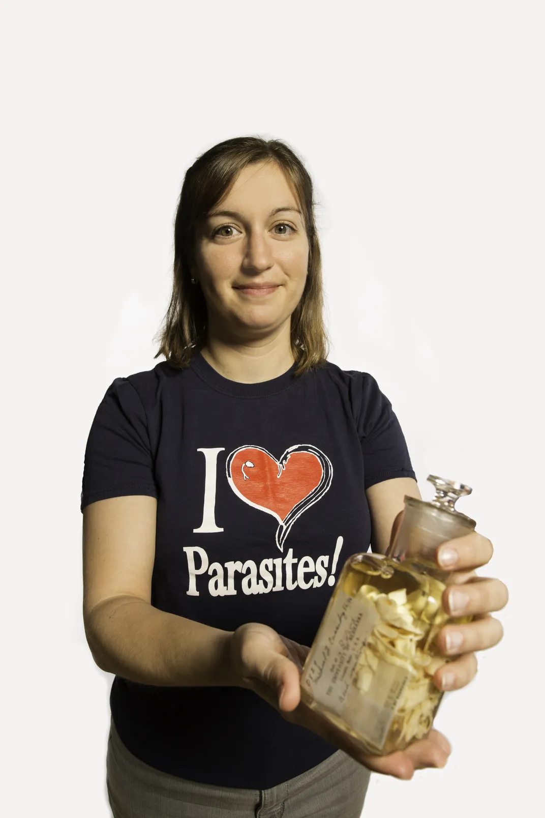 Smithsonian Curator Anna Phillips wearing a black shirt that reads "I heart parasites" and holding a jar of parasitic worm specimens.  