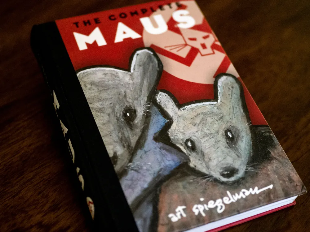 A hardcover edition of Maus, with two gray mice on its cover in front of a red background and swastika symbol