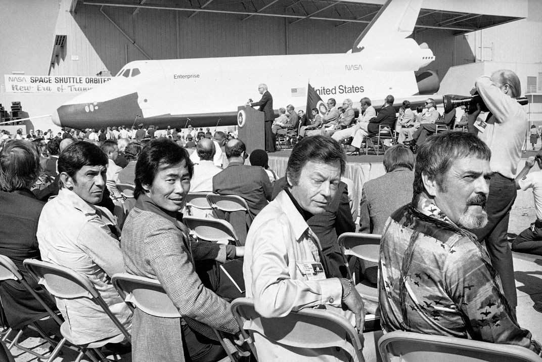 Leonard Nimoy, George Takei, DeForest Kelley, and James Doohan seated in a crowd