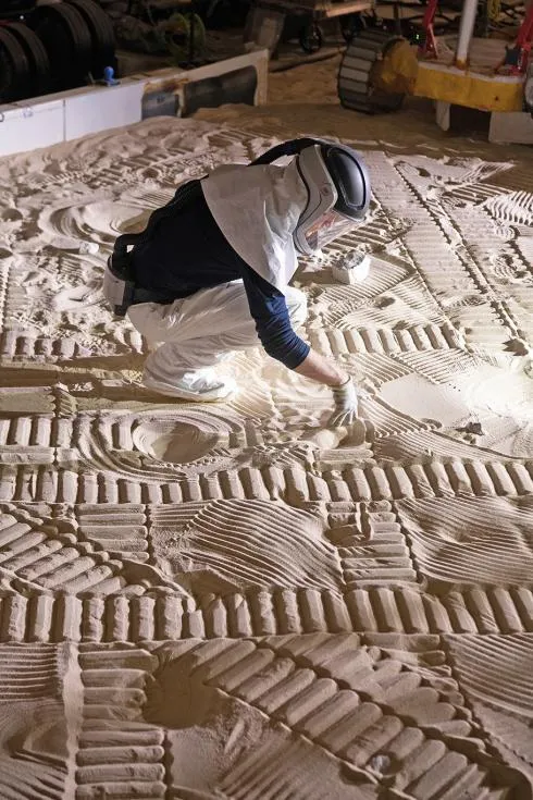 A scientist leans down over light brown sand covered with circular depressions and track marks."