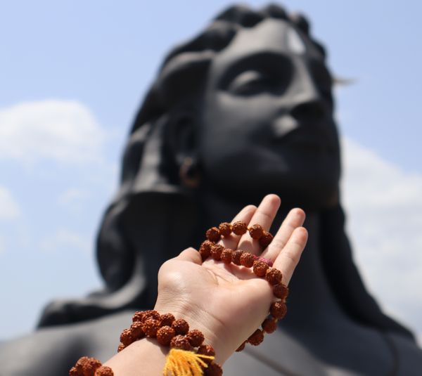 The lady's hand is wrapped around a Rudraksha garland and prays to the Indian God adi yogi Shiva statue, who holds a place in the Guinness World Record. thumbnail